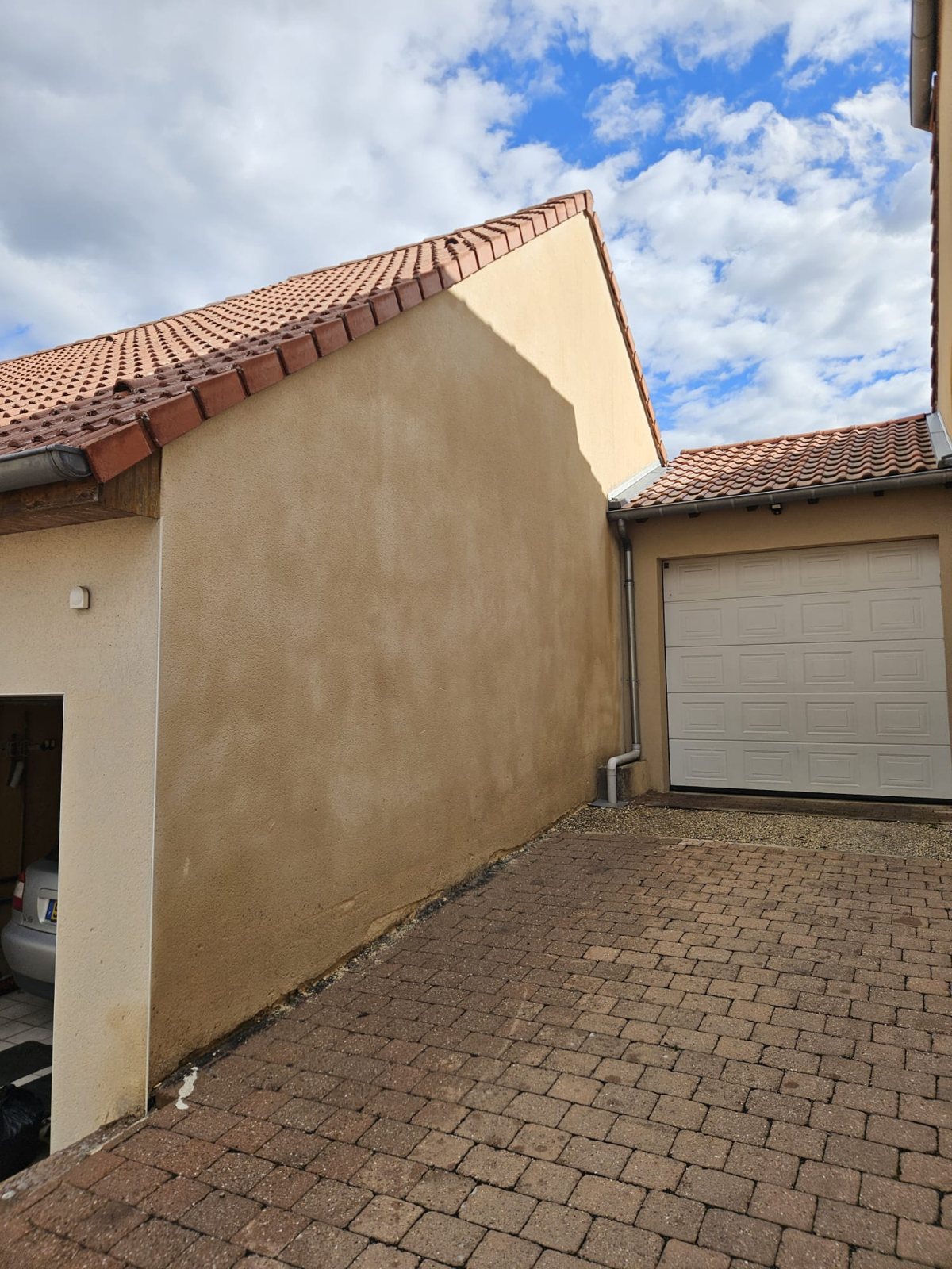 Pignon de maison au crépi beige, propre, au-dessus d'une cour pavée.