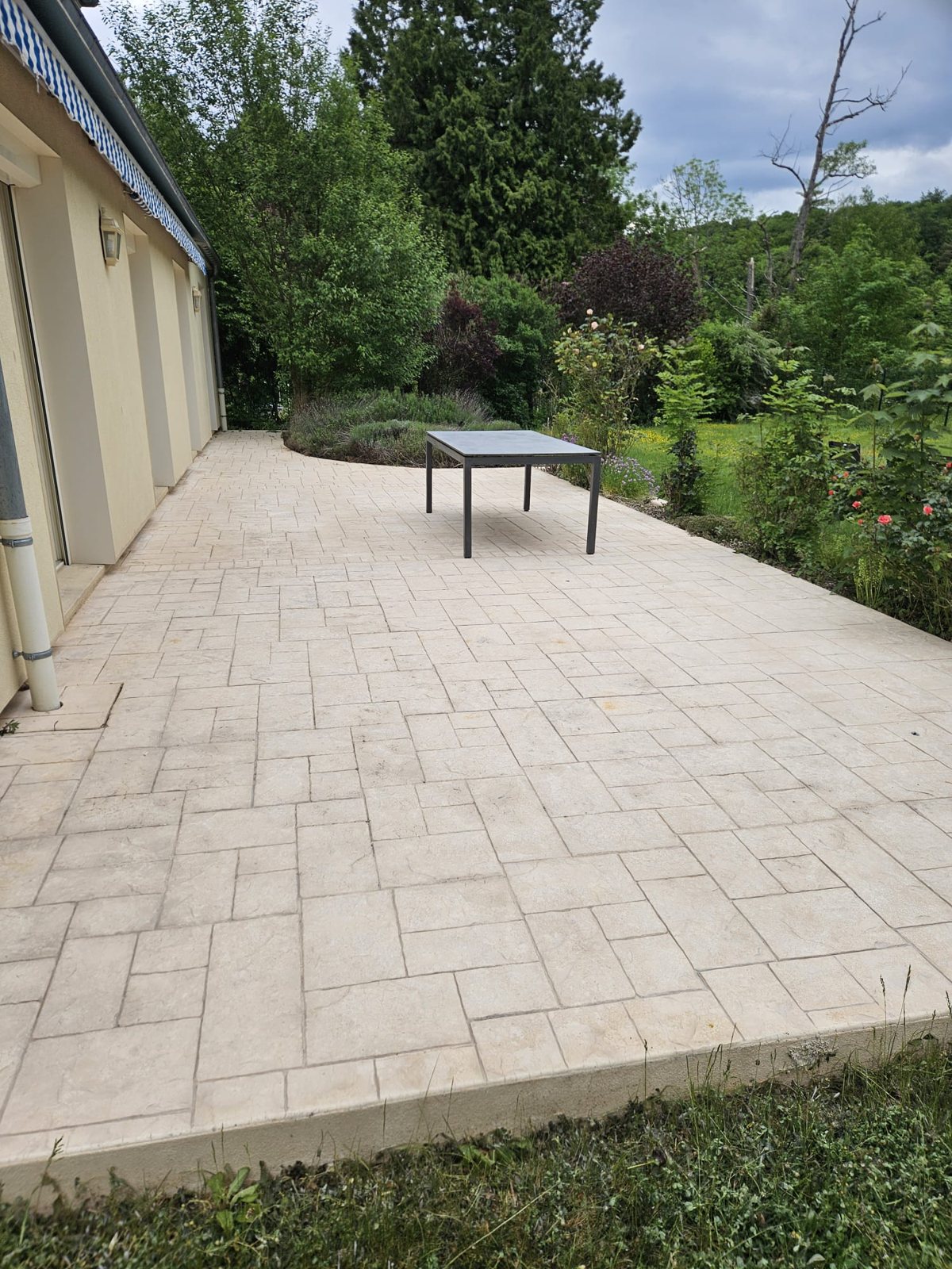 Grande terrasse en dalles claires, propre, avec une table de jardin.