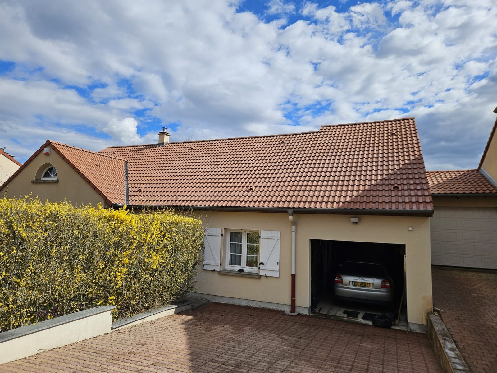 Toiture de pavillon en tuiles rouges, propre, au-dessus d'une haie fleurie.